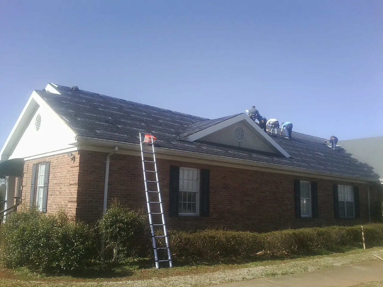 Crew tearing shingles off a brick ranch roof with a ladder set — Emergency Roof Repair work by our crew in Fords