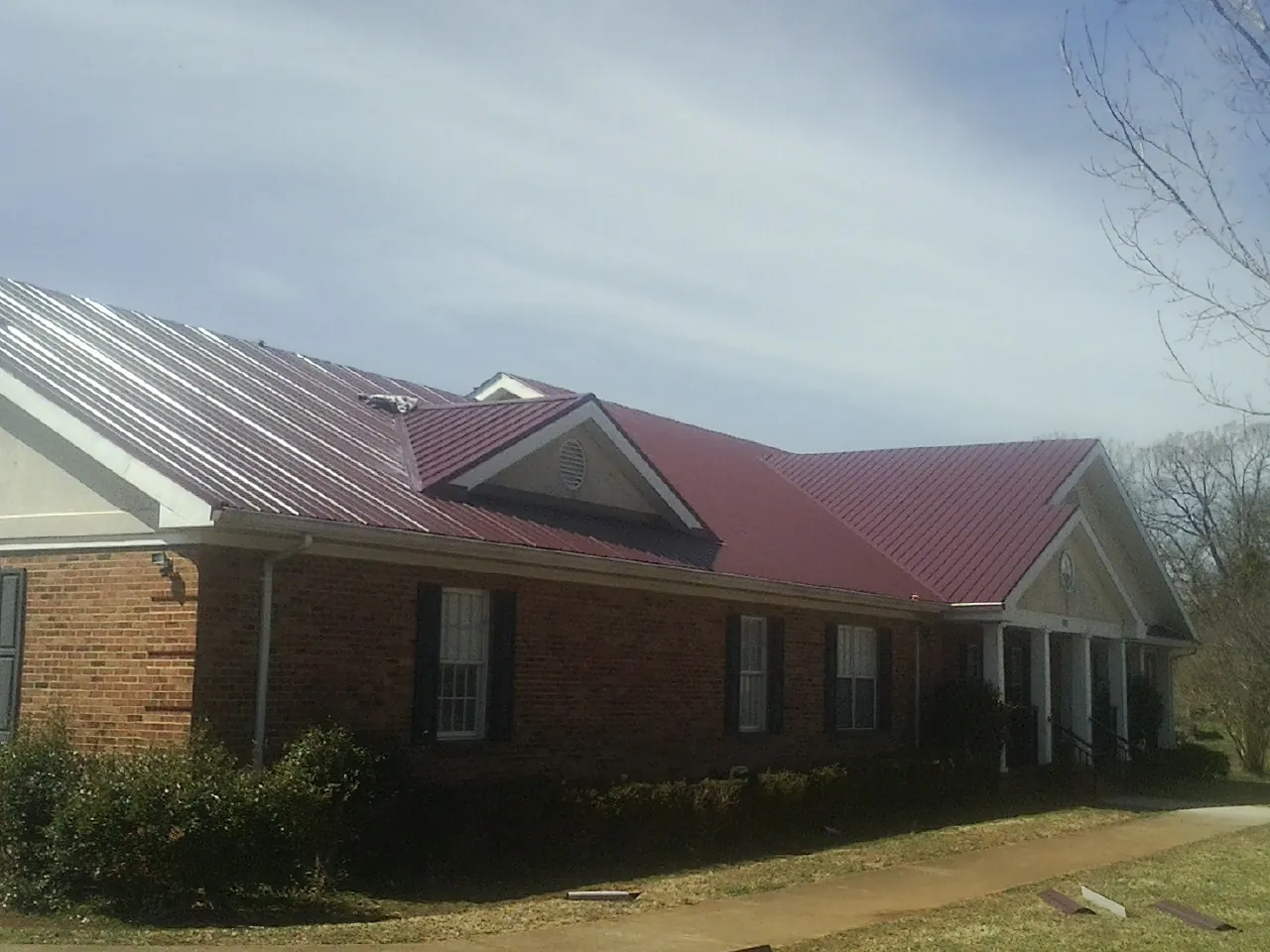 Red metal roof with gabled entries on a long brick building, from a Hail Damage Roof Repair job in Fords