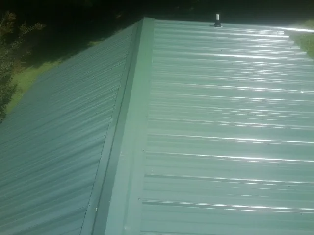 New green metal panels meeting at the ridge of a roof — Flat Roof Repair work by our crew in Fords