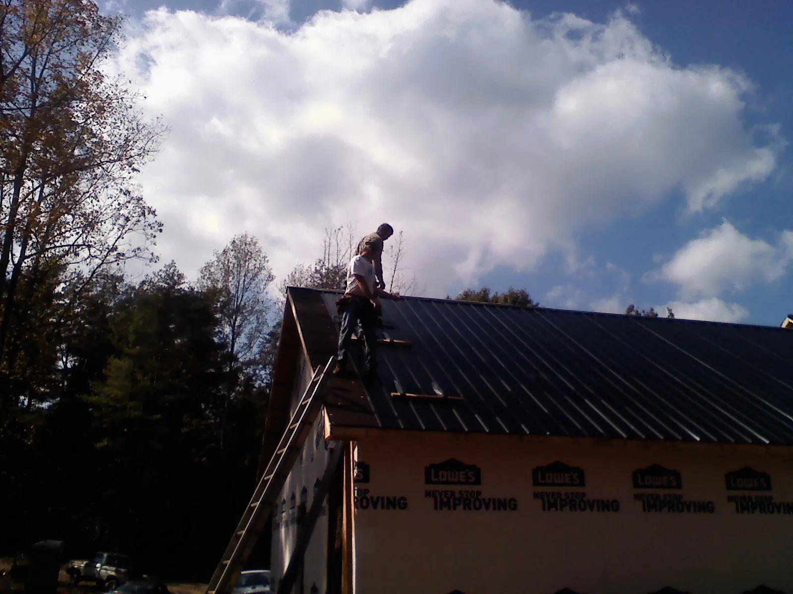 Roofer fastening dark metal panels high against a cloudy sky, from a Roof Inspection job in Fords